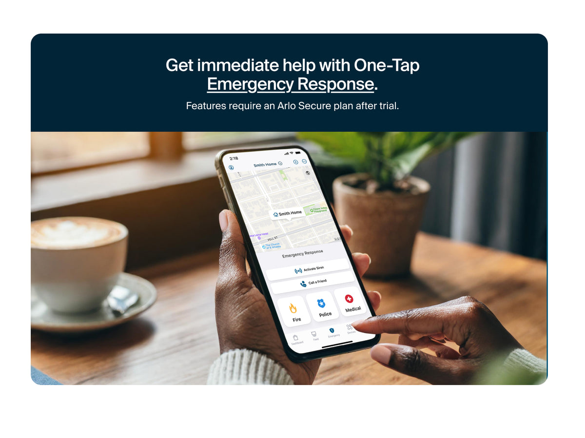 Person using a smartphone with emergency response Arlo Secure app on a table with a cup of coffee and plant.